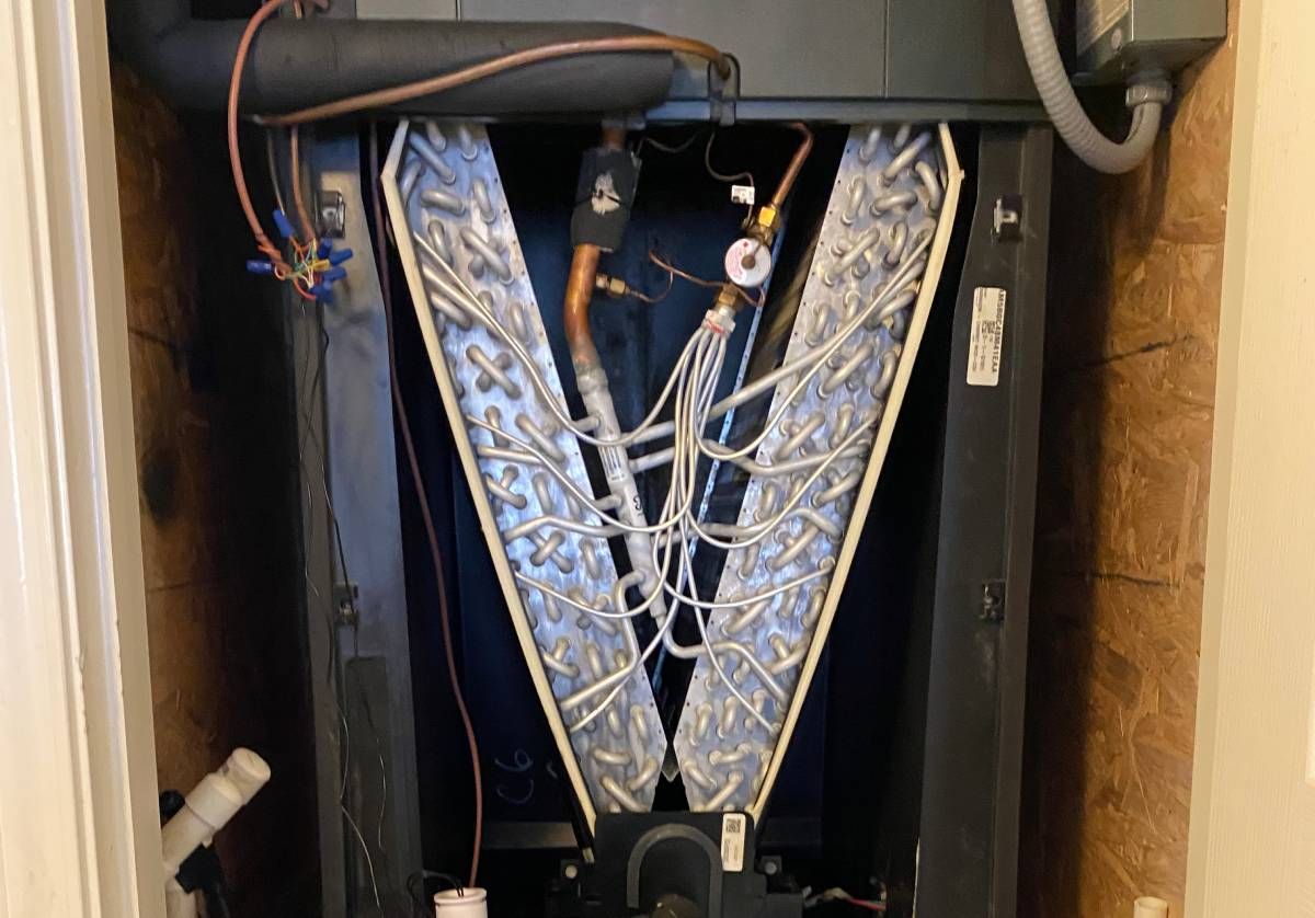 Open HVAC unit with V-shaped metal coils and wiring inside a cabinet