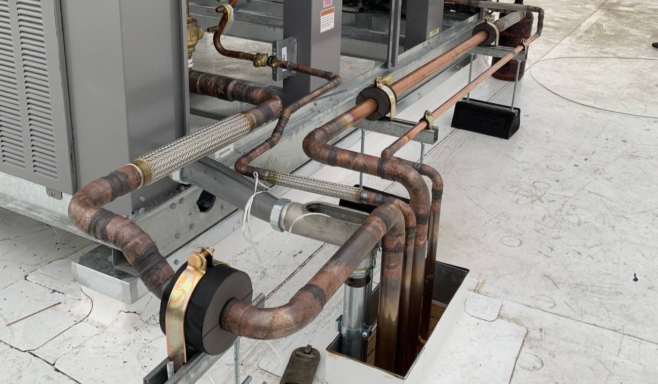 Rusty insulated pipes and metal ducts running beside outdoor HVAC equipment on a concrete rooftop.