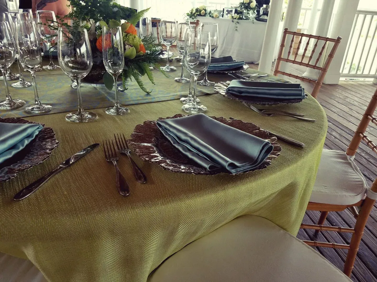 A table set for a formal event with gold tablecloths, metallic charger plates, grey napkins, and wine glasses.
