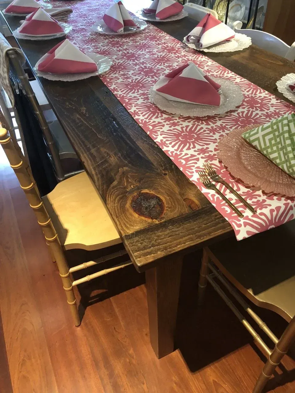 A rustic wooden dining table set with white plates, folded pink napkins, and a pink and white patterned runner.