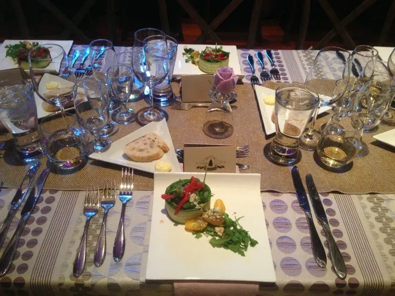 A table setting for fine dining, with white square plates featuring fresh salads, bread, glassware, and silver cutlery.