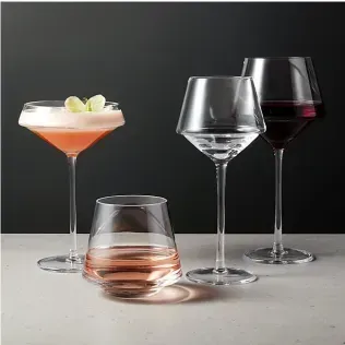 Four distinct glassware pieces, including stemmed glasses and a tumbler, holding varied drinks against a dark backdrop.