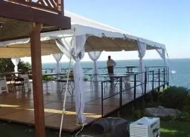 A covered outdoor deck overlooking the ocean with a dance floor, white draping, and a person standing by the railing.