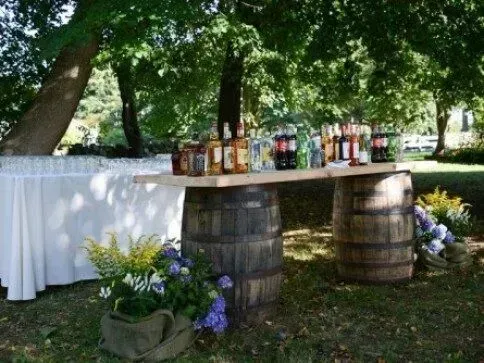 A bar setup in a garden, with drinks arranged on a wooden board balanced atop two rustic whiskey barrels.