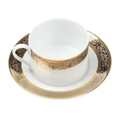 A white porcelain teacup and saucer decorated with a decorative gold and black ornate filigree pattern.