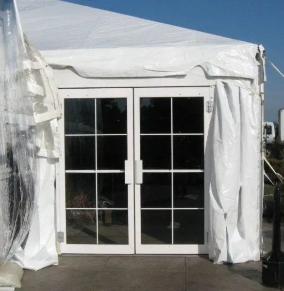 Double glass doors with white frames and grid patterns, set within a white tent structure on a paved surface.
