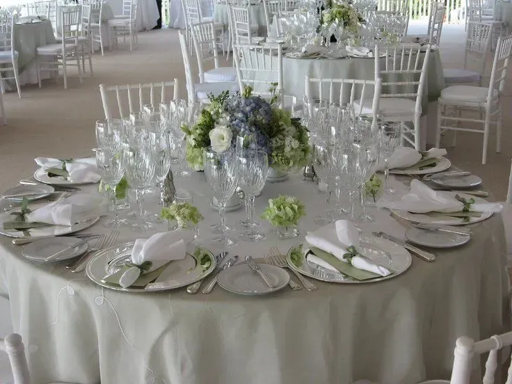 A round banquet table set for a formal event with white linens, china, crystal glasses, and a floral centerpiece.