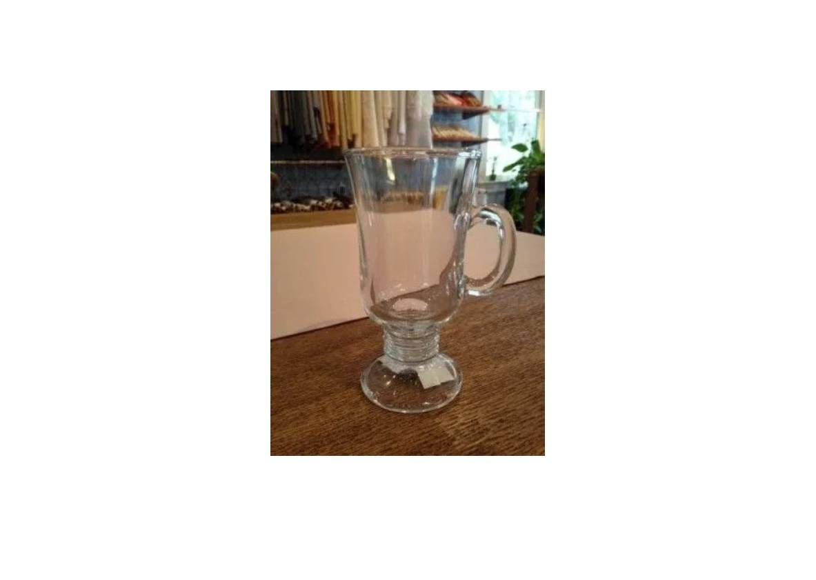 A clear glass Irish coffee mug with a sturdy base and a side handle, sitting on a wooden surface.