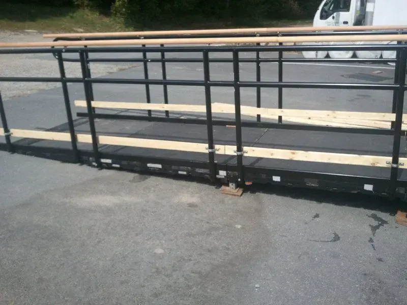 A portable black metal wheelchair ramp with wooden side rails and handrails sitting on a paved surface.