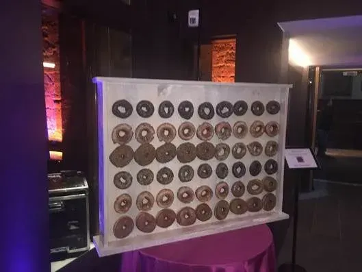 A large rectangular display board holding rows of glazed doughnuts, set on a table in a dimly lit indoor event space.