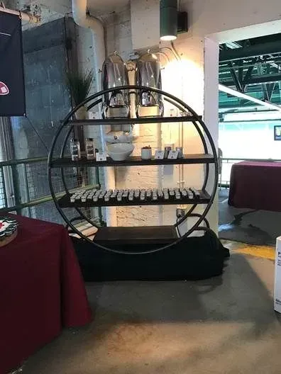 A circular, tiered metal shelf stands in a room, displaying small items and neatly arranged white rectangular objects.