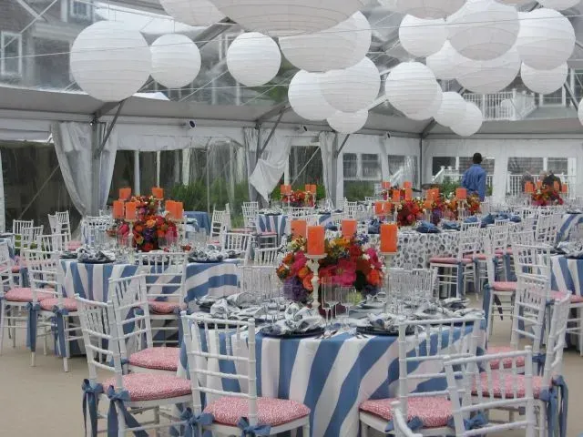 An outdoor event tent set with tables featuring blue and white striped tablecloths, floral centerpieces, and white chairs.