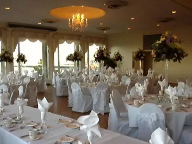 A banquet hall set for a formal event with round tables, white tablecloths, floral centerpieces, and white chair covers.