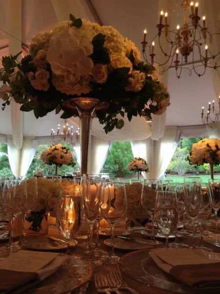 A formal dining table set for an event with tall floral centerpieces, candles, glassware, and draped fabric in the back.
