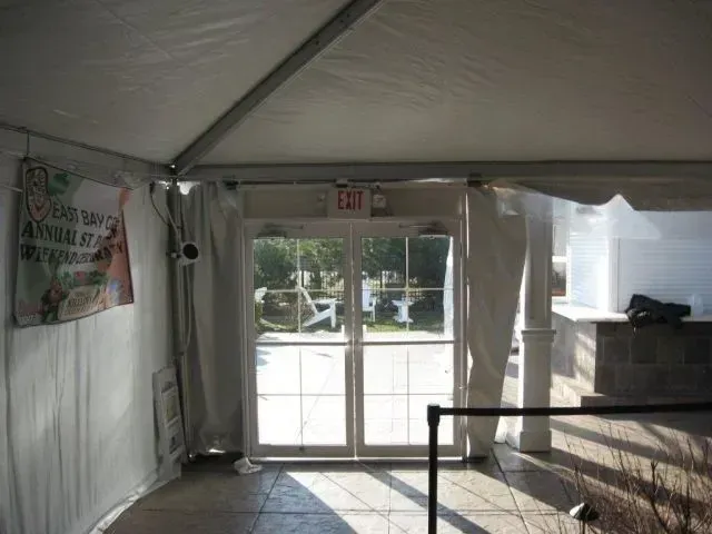A view from inside a tent looking out through glass double doors at a patio, with an exit sign above the doorway.