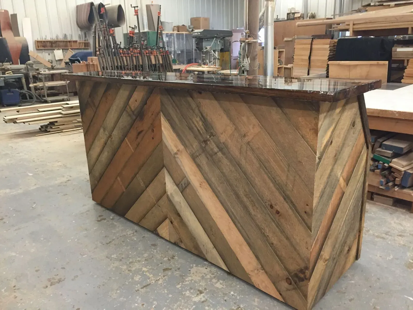 A custom bar counter in a workshop, featuring a chevron-patterned facade made from reclaimed, multi-toned wood planks.