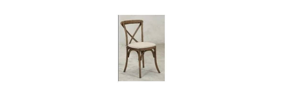 A wooden cross-back chair with a light-colored, upholstered seat on a neutral background.
