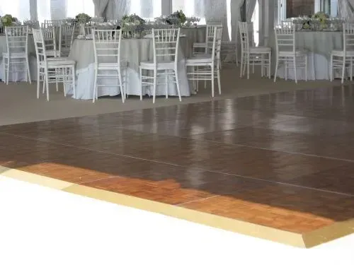 A dark wooden dance floor in the foreground, with tables and white chairs set up for a formal event in the background.