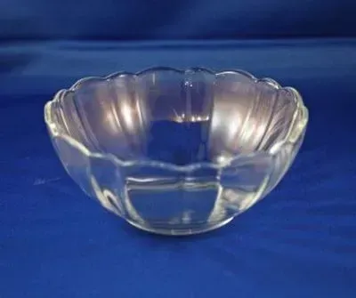 A clear, scalloped glass bowl sits centered on a solid blue background.