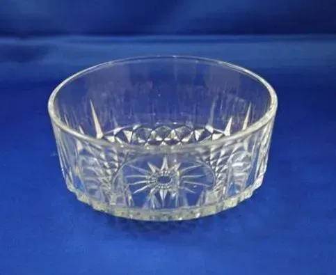 A clear, round glass serving bowl with a faceted, diamond-cut pattern and a starburst design on the base.