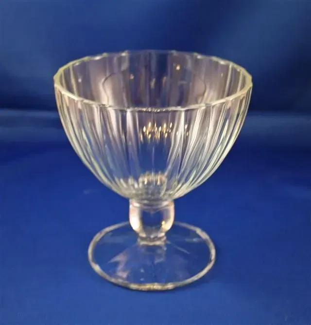 A clear glass footed dessert bowl with vertical fluted ribs, centered against a plain blue background.