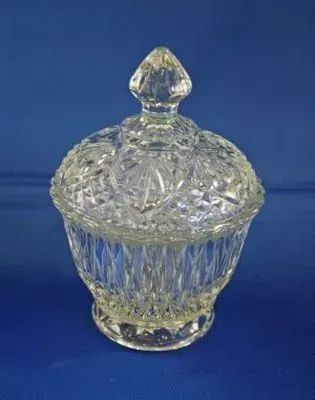 A clear, crystal lidded candy dish with a diamond-cut pattern, set against a solid blue background.