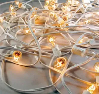 A tangled pile of glowing, warm-toned string lights with white cords against a light-colored background.