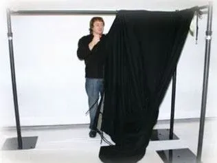 A person sets up a black backdrop on a portable metal stand in a white room.