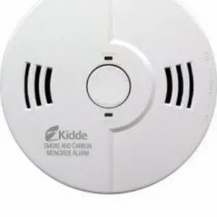 A white, circular Kidde brand smoke and carbon monoxide alarm mounted on a wall.