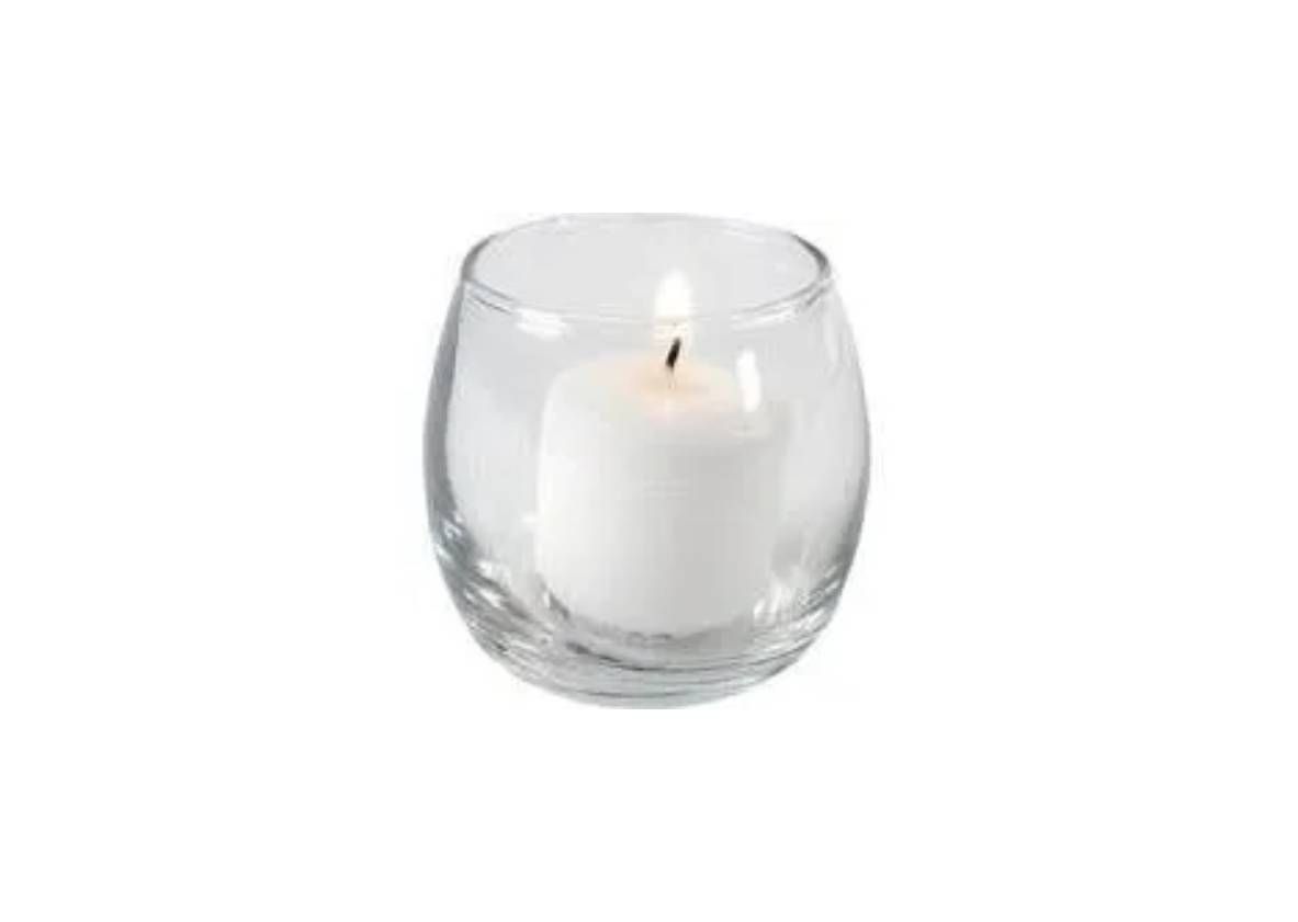 A small, white pillar candle with a lit flame inside a clear, round glass votive holder.