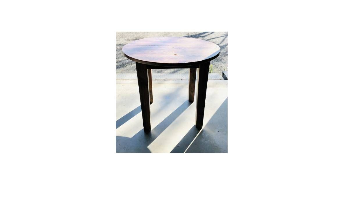 A small, round, dark wood side table with four straight legs standing on a smooth, light-colored floor.