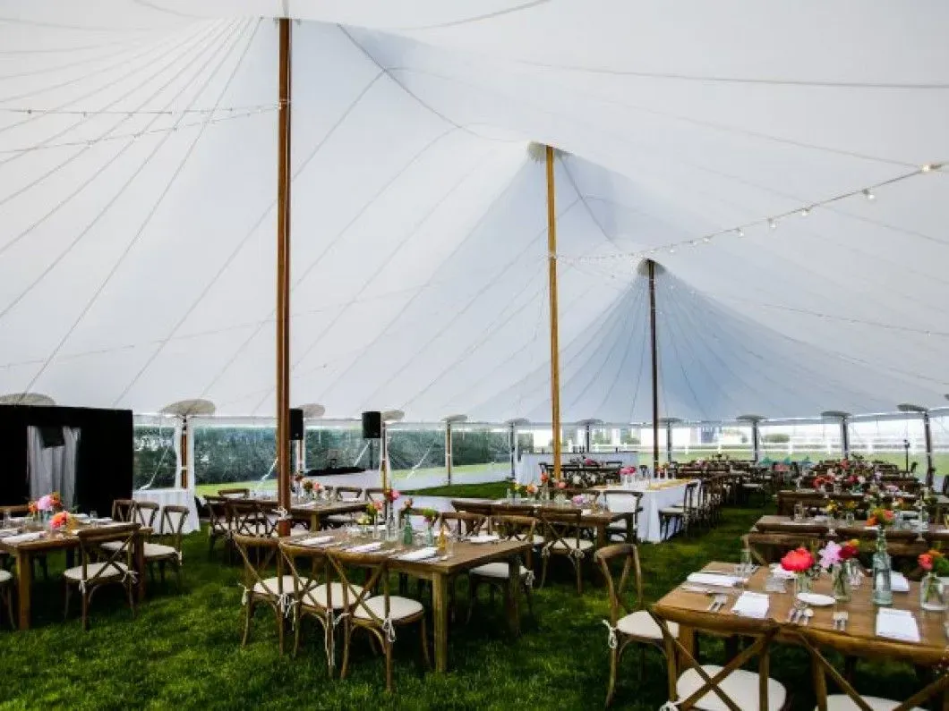 A large white event tent featuring wooden poles and rows of tables with chairs set up for a celebration on a grassy lawn.