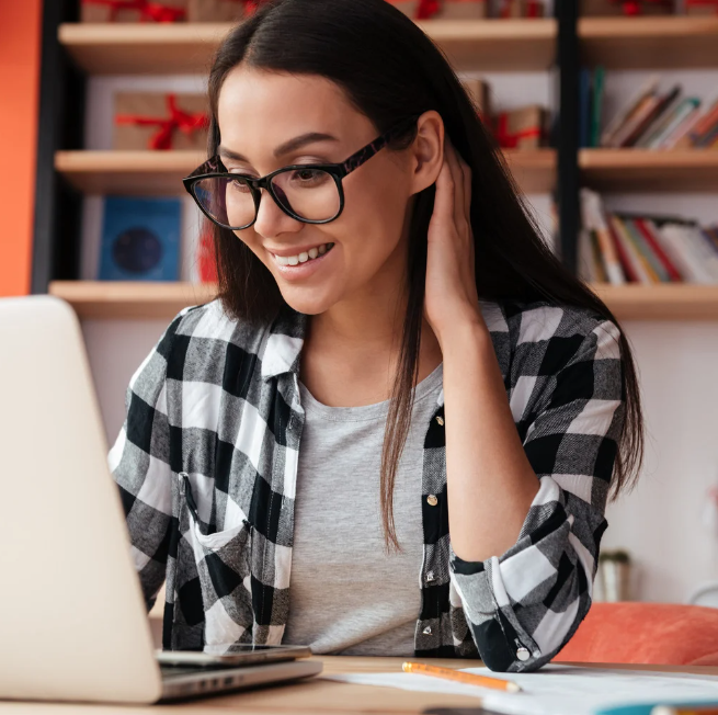 A woman wearing glasses is sitting at a desk using a laptop computer.