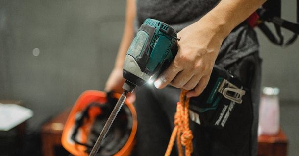 A person is holding a drill and a helmet in their hands.