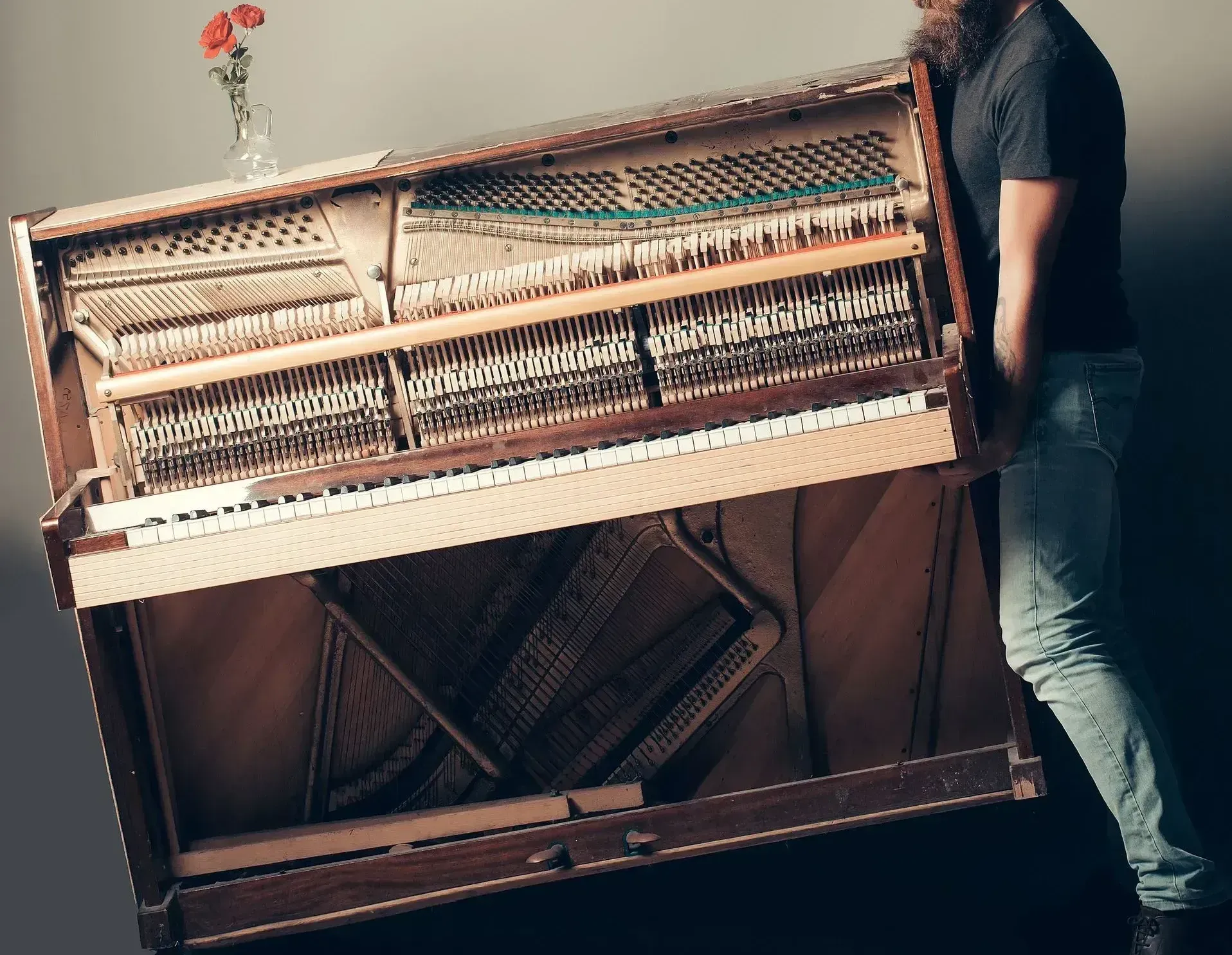 A man is carrying a piano with a flower in a vase on top of it