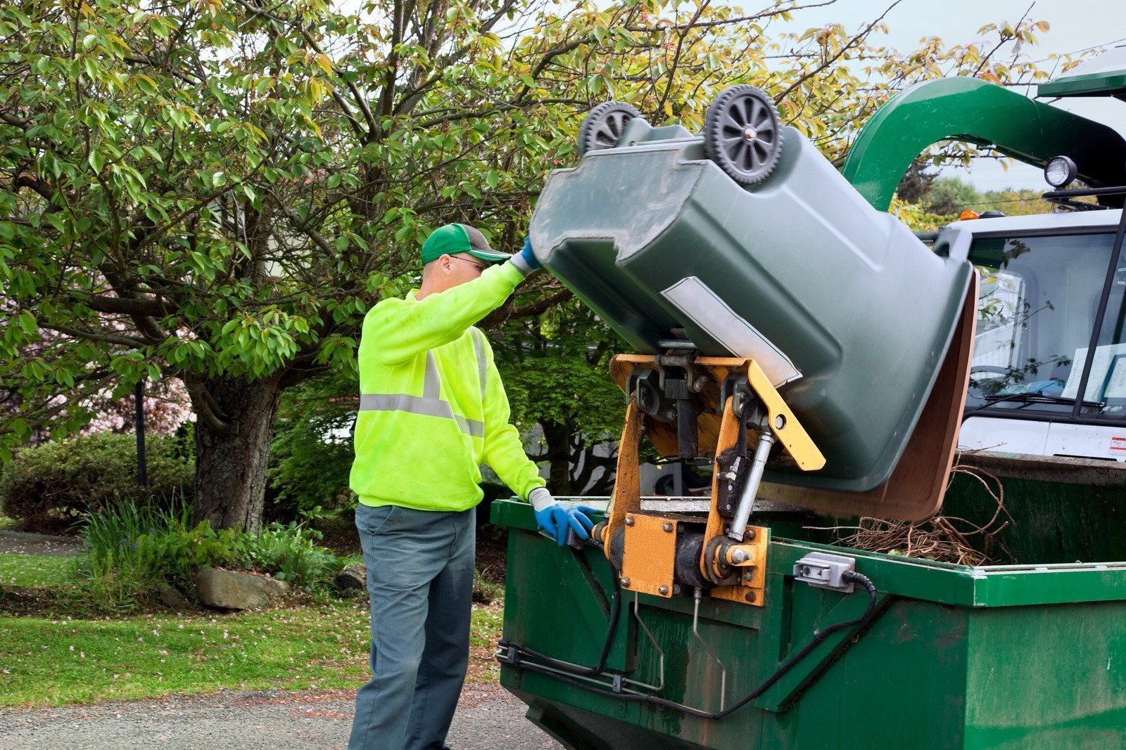 A man is loading a trash can into a garbage truck.
