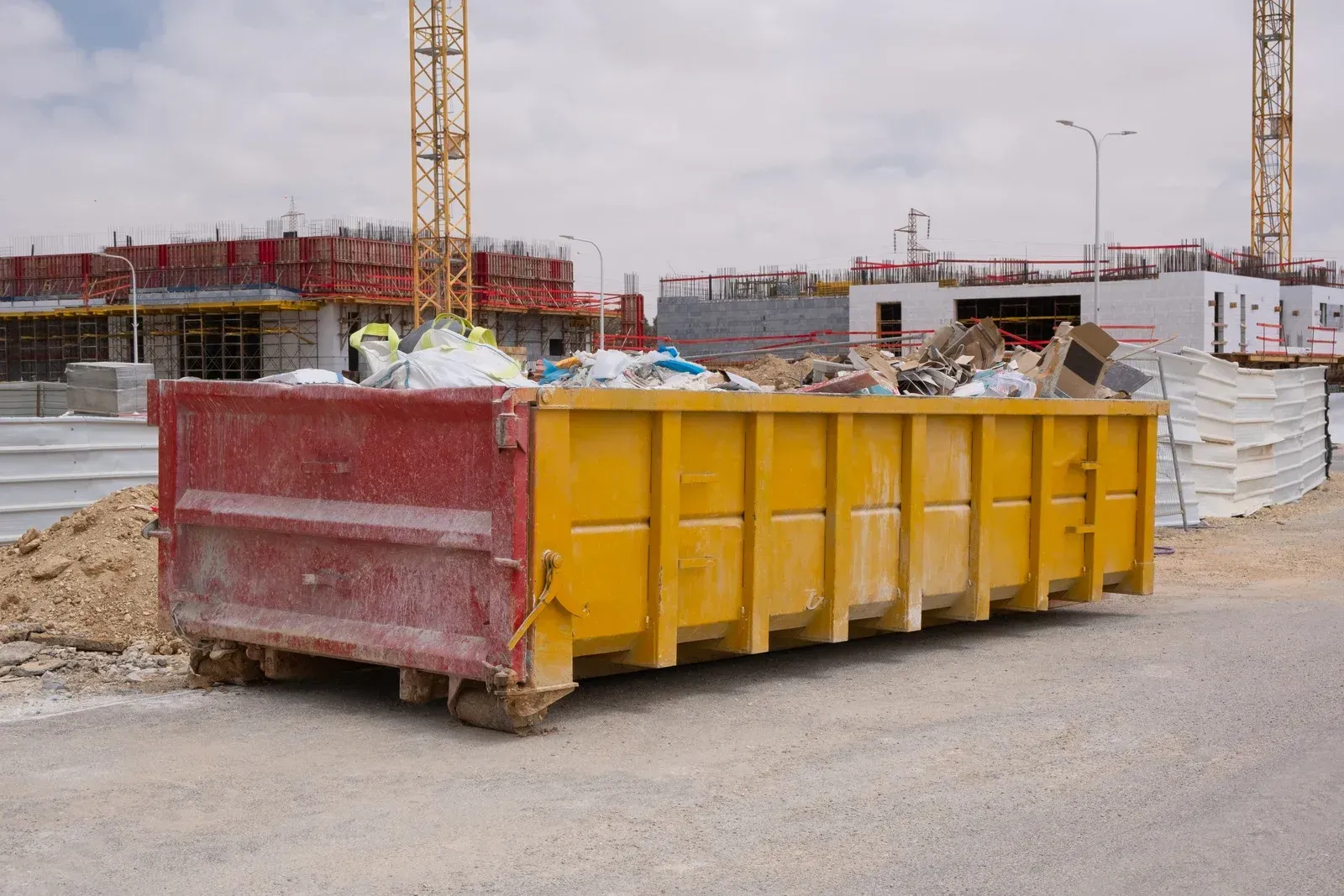 A large yellow dumpster is parked in front of a construction site.