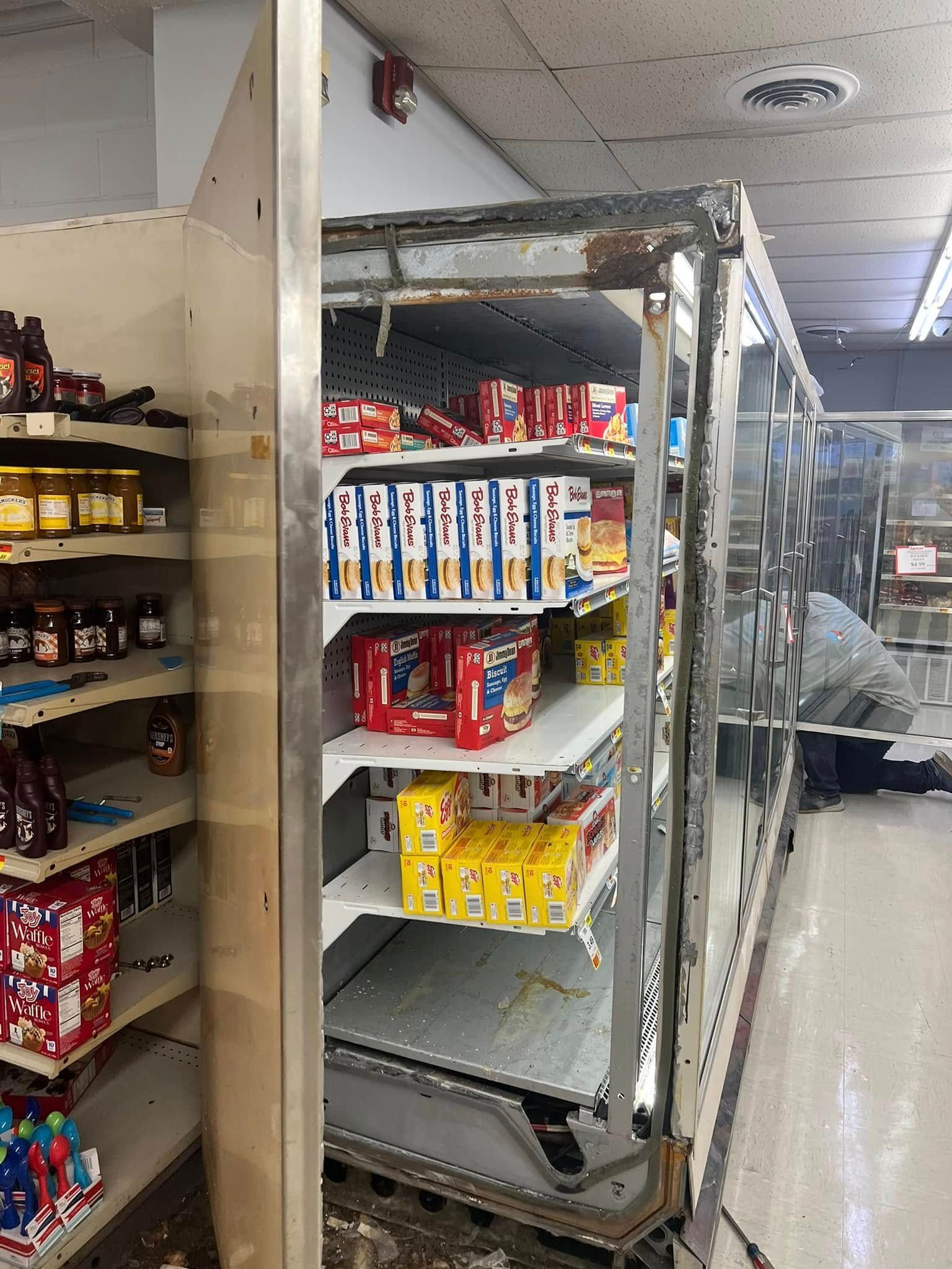 A commercial refrigerator display with missing doors and shelves stocked with various food products in a grocery store.