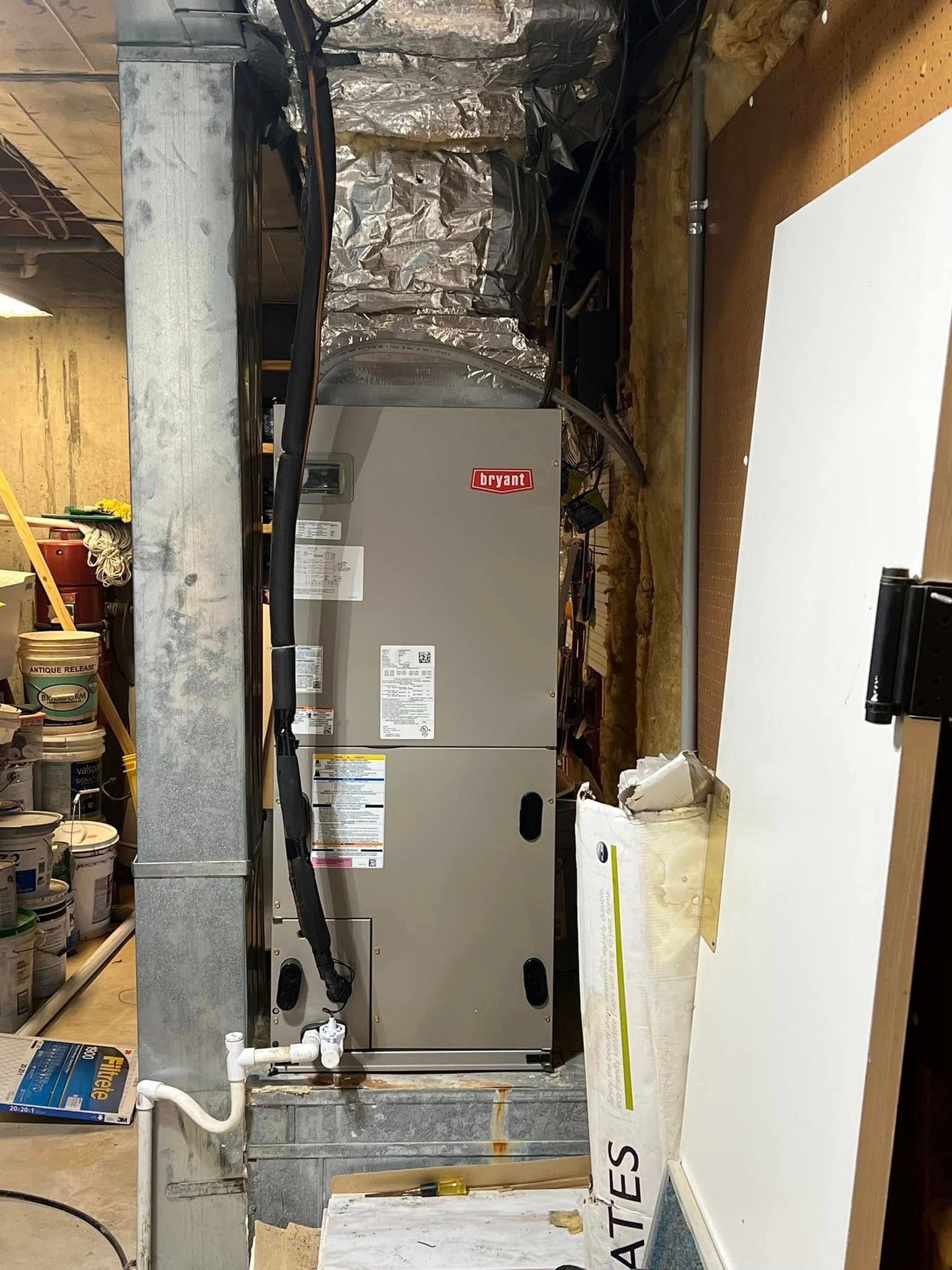 A grey HVAC air handler unit installed in a utility closet with silver foil-wrapped ductwork above it.