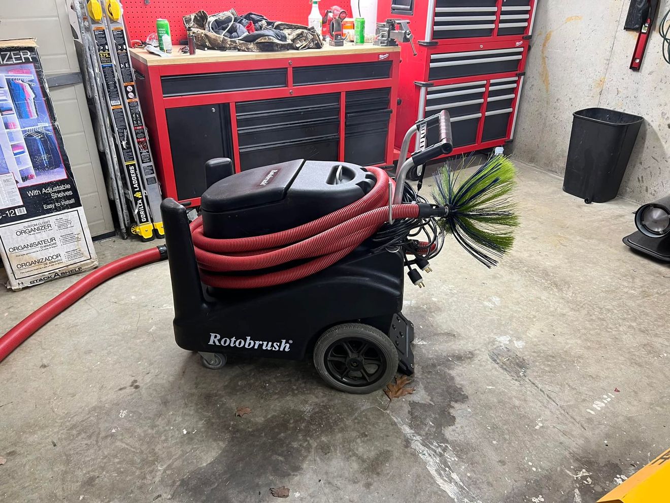 A black Rotobrush air duct cleaning machine with a red hose and attached brush in a workshop.
