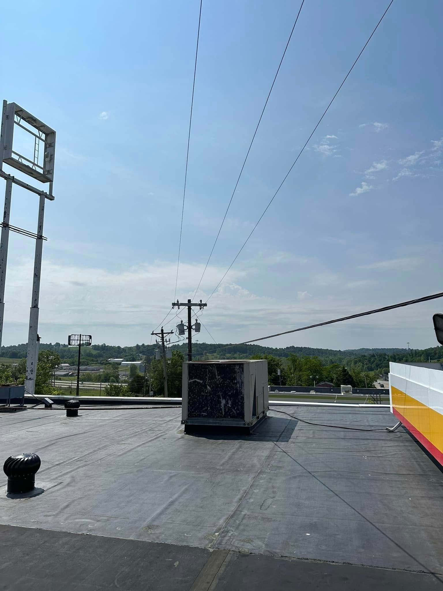 A flat commercial rooftop view with a rectangular HVAC unit, power lines overhead, and a tall sign frame against a blue sky.