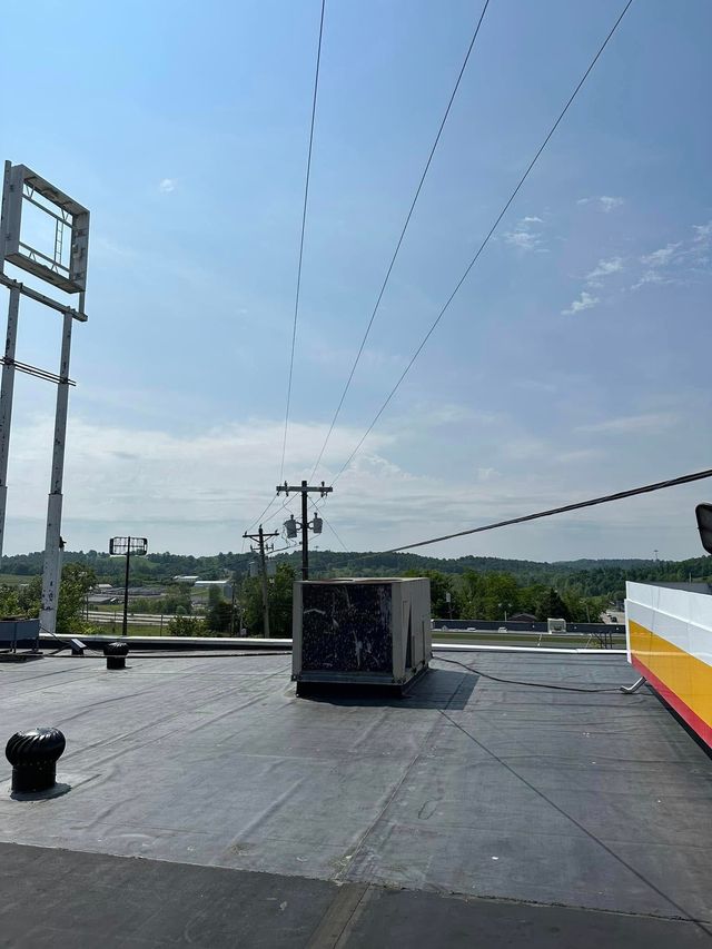 A flat commercial rooftop view with a rectangular HVAC unit, power lines overhead, and a tall sign frame against a blue sky.