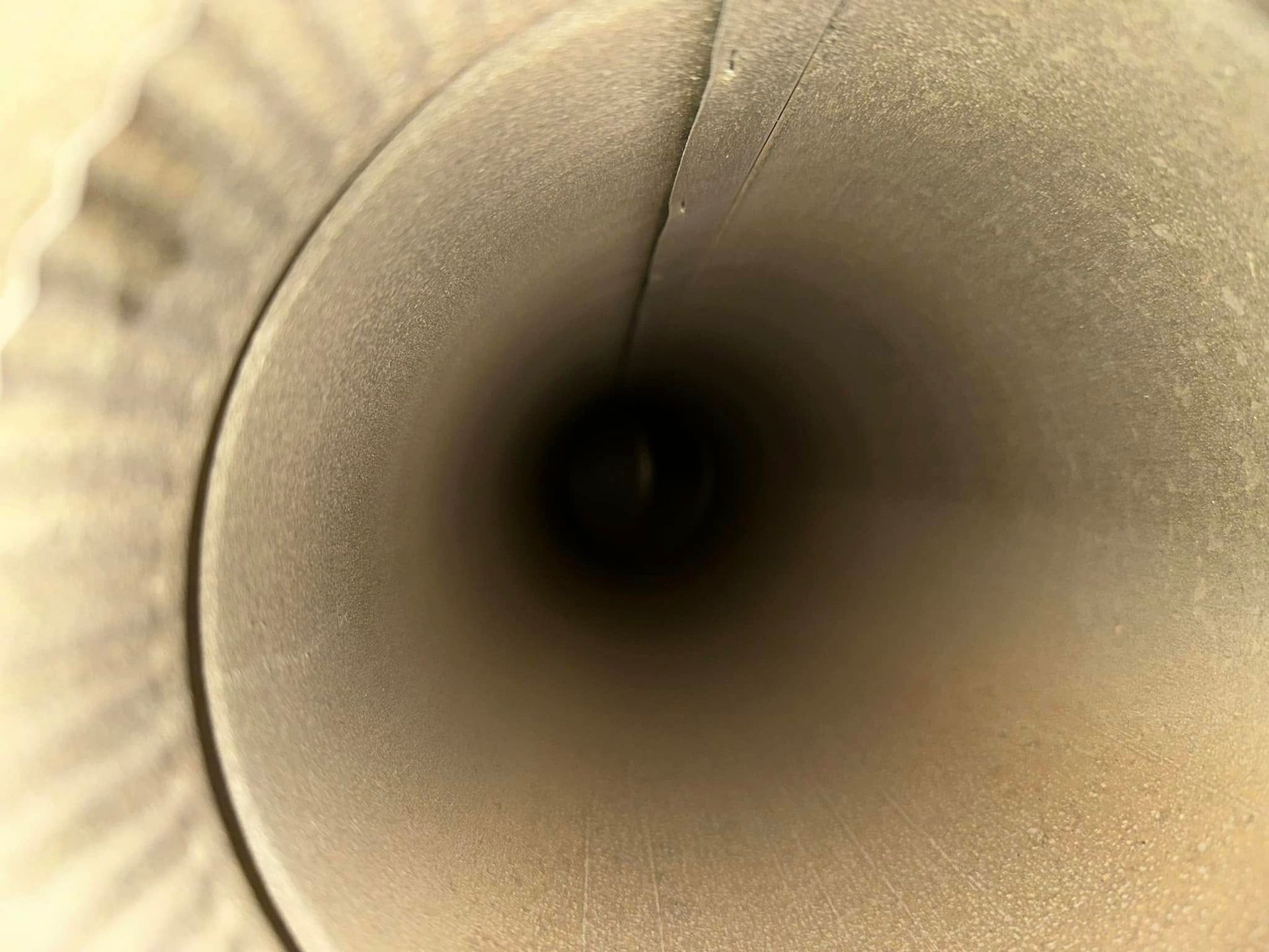 A view looking into a cylindrical metal pipe or chimney, showing a smooth interior surface and a dark opening at the end.