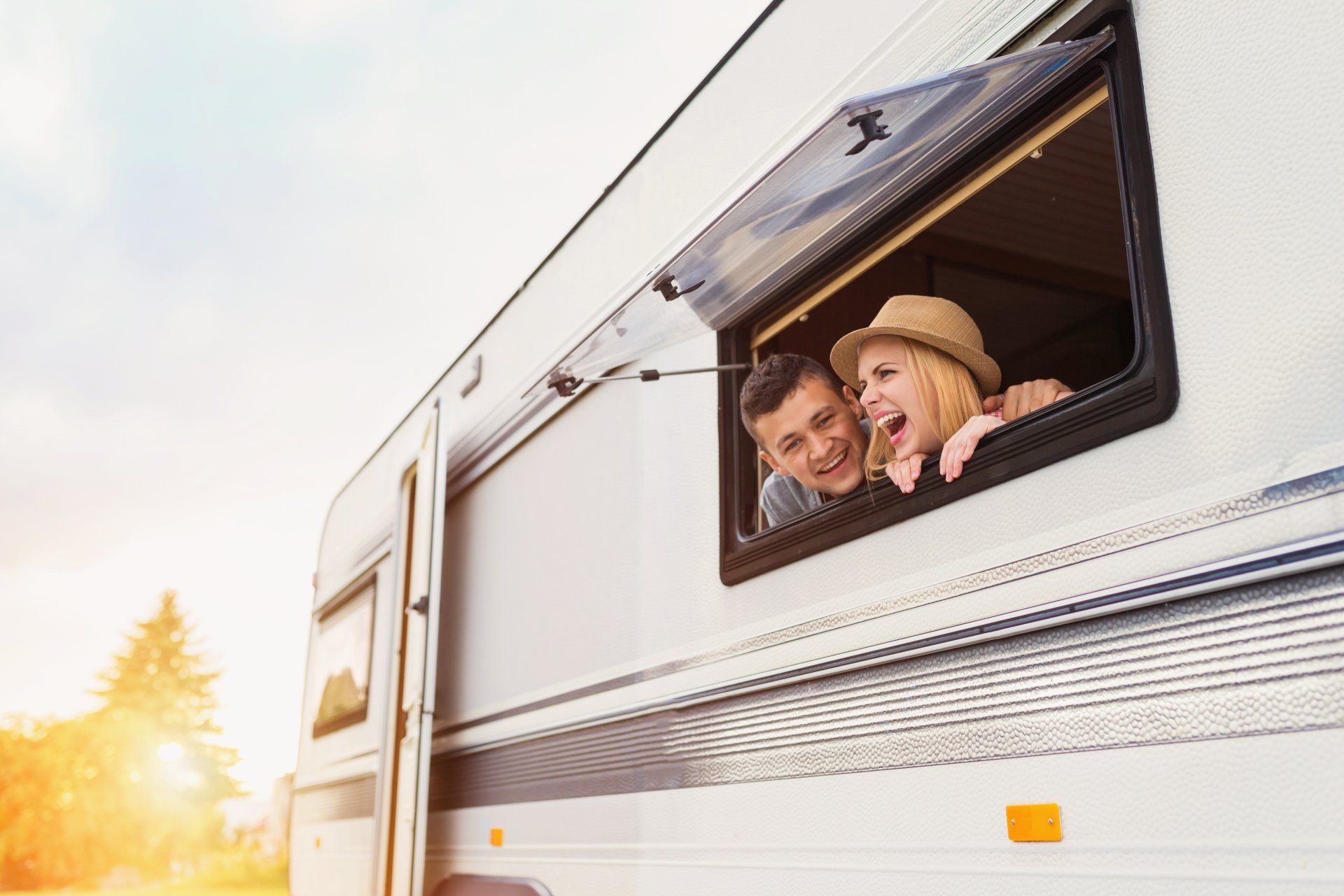 Young Couple Smiling Through Open Caravan Window — Caravan Experts In The Charters Towers Region, QLD