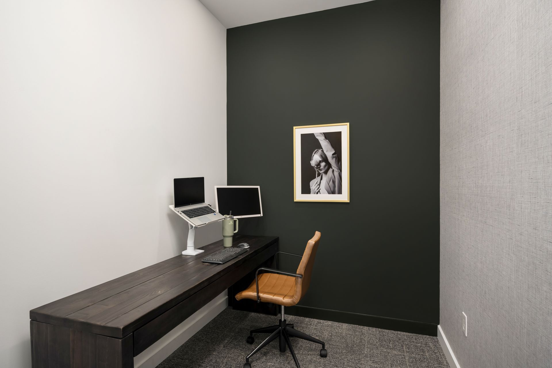 a small office with a desk , chair , computer and laptop .