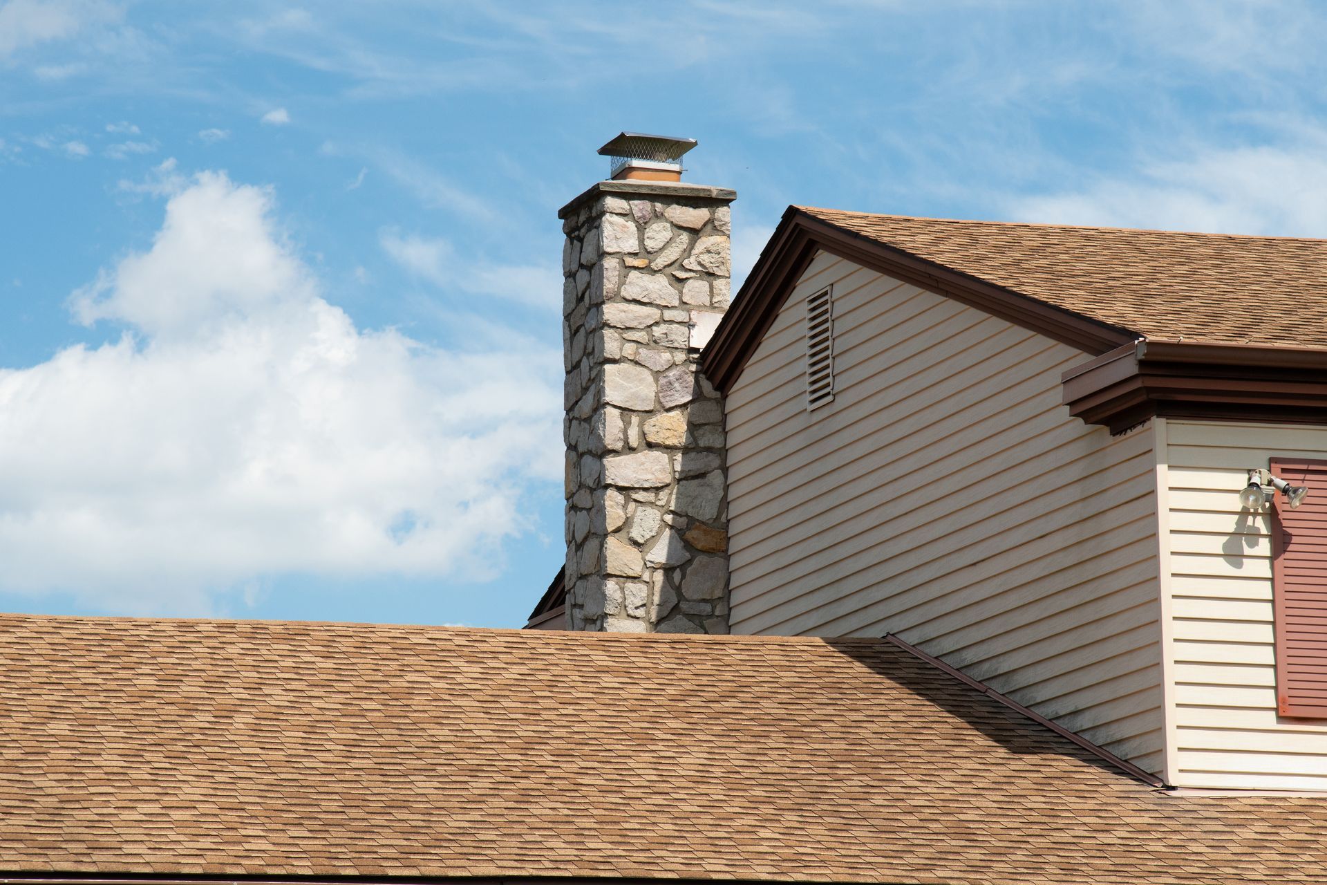 Brick chimney on a red tile roof against a blue sky