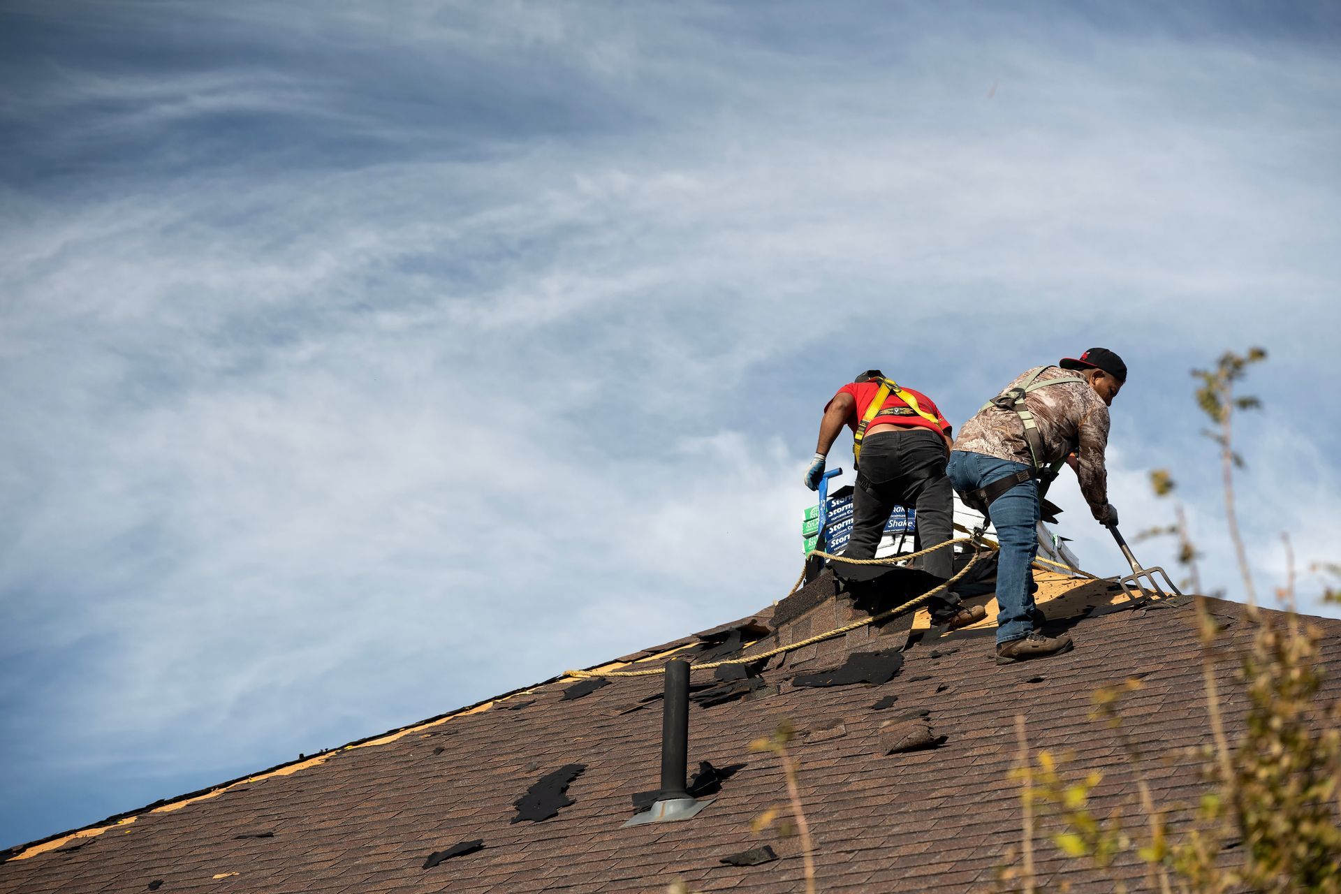 Two roofers working on a shingled rooftop under a cloudy sky