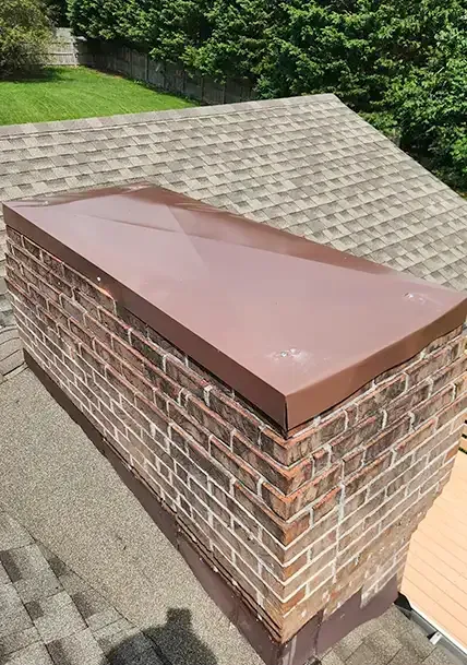Brick chimney with a brown metal cap on a shingled roof, viewed from above.