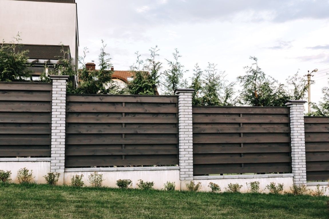 Dark brown horizontal wooden fence with white stone pillars and green grass.
