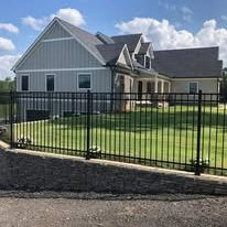 A house with gray siding behind a black metal fence by Henderson Fence on a sunny day.